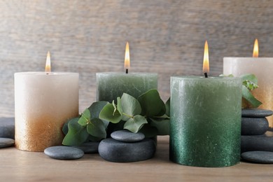Photo of Burning candles, stones and eucalyptus branches on wooden table, closeup