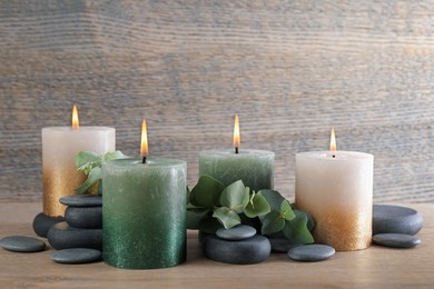 Photo of Burning candles, stones and eucalyptus branches on wooden table