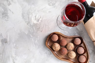 Photo of Delicious truffle bonbons and red wine on light grey background, flat lay. Space for text