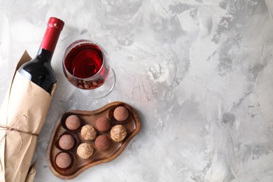 Photo of Delicious truffle bonbons and red wine on light grey background, flat lay. Space for text