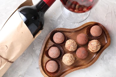 Photo of Delicious truffle bonbons and red wine on light grey background, flat lay