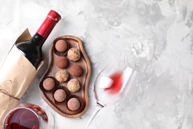 Photo of Delicious truffle bonbons and red wine on light grey background, flat lay. Space for text