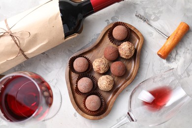 Photo of Delicious truffle bonbons and red wine on light grey background, flat lay