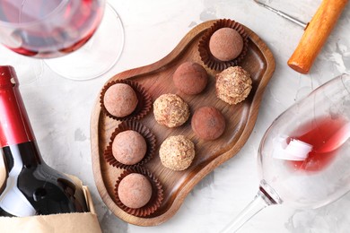 Photo of Delicious truffle bonbons and red wine on light grey background, flat lay