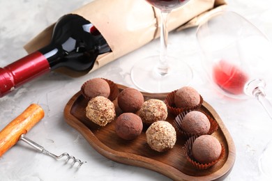 Photo of Delicious truffle bonbons and red wine on light grey background, closeup