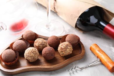 Photo of Delicious truffle bonbons and red wine on light grey background, closeup