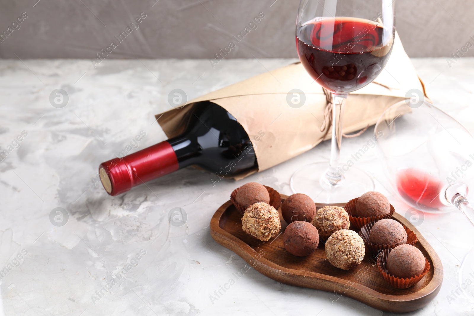 Delicious truffle bonbons and red wine on light grey background Photo of Delicious truffle bonbons and red wine on light grey background