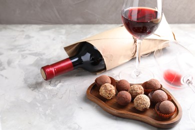 Photo of Delicious truffle bonbons and red wine on light grey background