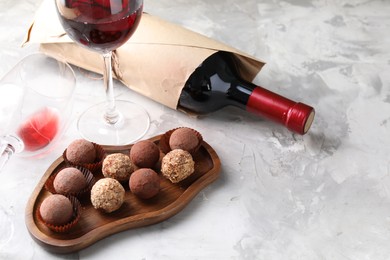 Photo of Delicious truffle bonbons and red wine on light grey background, closeup