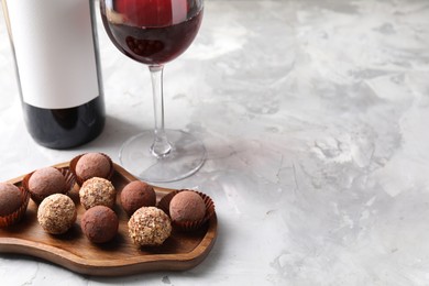 Photo of Delicious truffle bonbons and red wine on light grey background, closeup