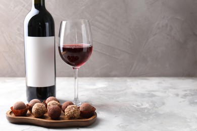 Photo of Delicious truffle bonbons and red wine on light grey background. Space for text