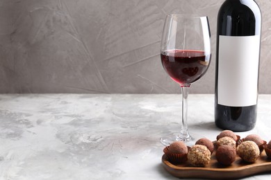 Photo of Delicious truffle bonbons and red wine on light grey background. Space for text