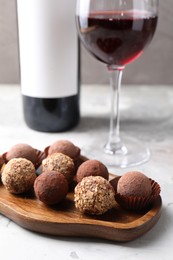 Photo of Delicious truffle bonbons and red wine on light grey background, closeup