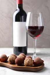 Photo of Delicious truffle bonbons and red wine on light grey background, closeup