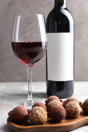 Photo of Delicious truffle bonbons and red wine on light grey background, closeup
