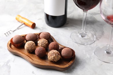 Photo of Delicious truffle bonbons and red wine on light grey background, closeup