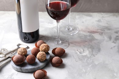 Photo of Delicious truffle bonbons and red wine on light grey background. Space for text