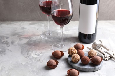 Photo of Delicious truffle bonbons and red wine on light grey background. Space for text