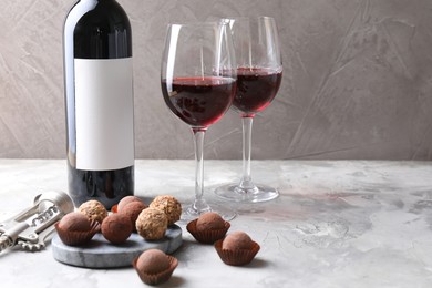 Photo of Delicious truffle bonbons and red wine on light grey background. Space for text
