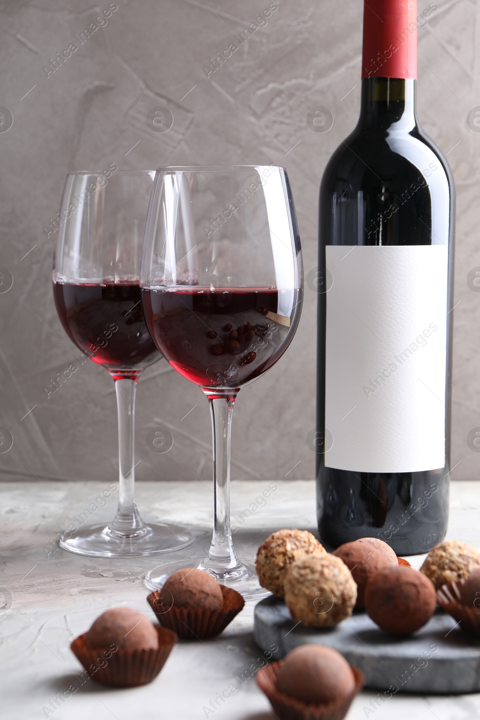 Photo of Delicious truffle bonbons and red wine on light grey background