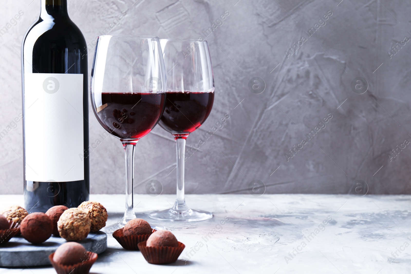 Delicious truffle bonbons and red wine on light grey background. Space for text Photo of Delicious truffle bonbons and red wine on light grey background. Space for text