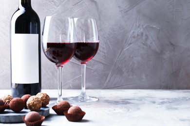 Photo of Delicious truffle bonbons and red wine on light grey background. Space for text