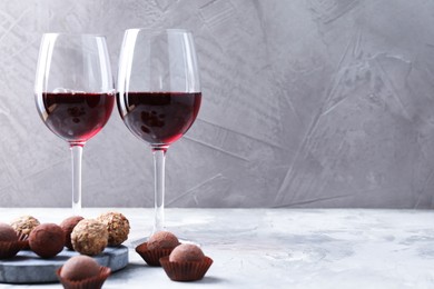 Photo of Delicious truffle bonbons and red wine on light grey background. Space for text
