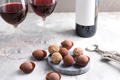 Photo of Delicious truffle bonbons and red wine on light grey background, closeup