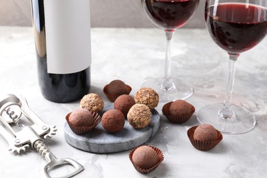 Photo of Delicious truffle bonbons and red wine on light grey background, closeup