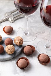 Photo of Delicious truffle bonbons and red wine on light grey background, closeup