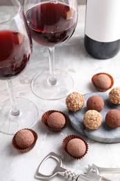 Photo of Delicious truffle bonbons and red wine on light grey background, closeup