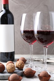 Photo of Delicious truffle bonbons and red wine on light grey background, closeup