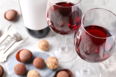Photo of Delicious truffle bonbons and red wine on light grey background, closeup