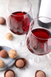 Photo of Delicious truffle bonbons and red wine on light grey background, closeup