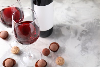 Photo of Delicious truffle bonbons and red wine on light grey background, closeup. Space for text
