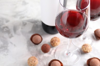 Photo of Delicious truffle bonbons and red wine on light grey background, closeup. Space for text