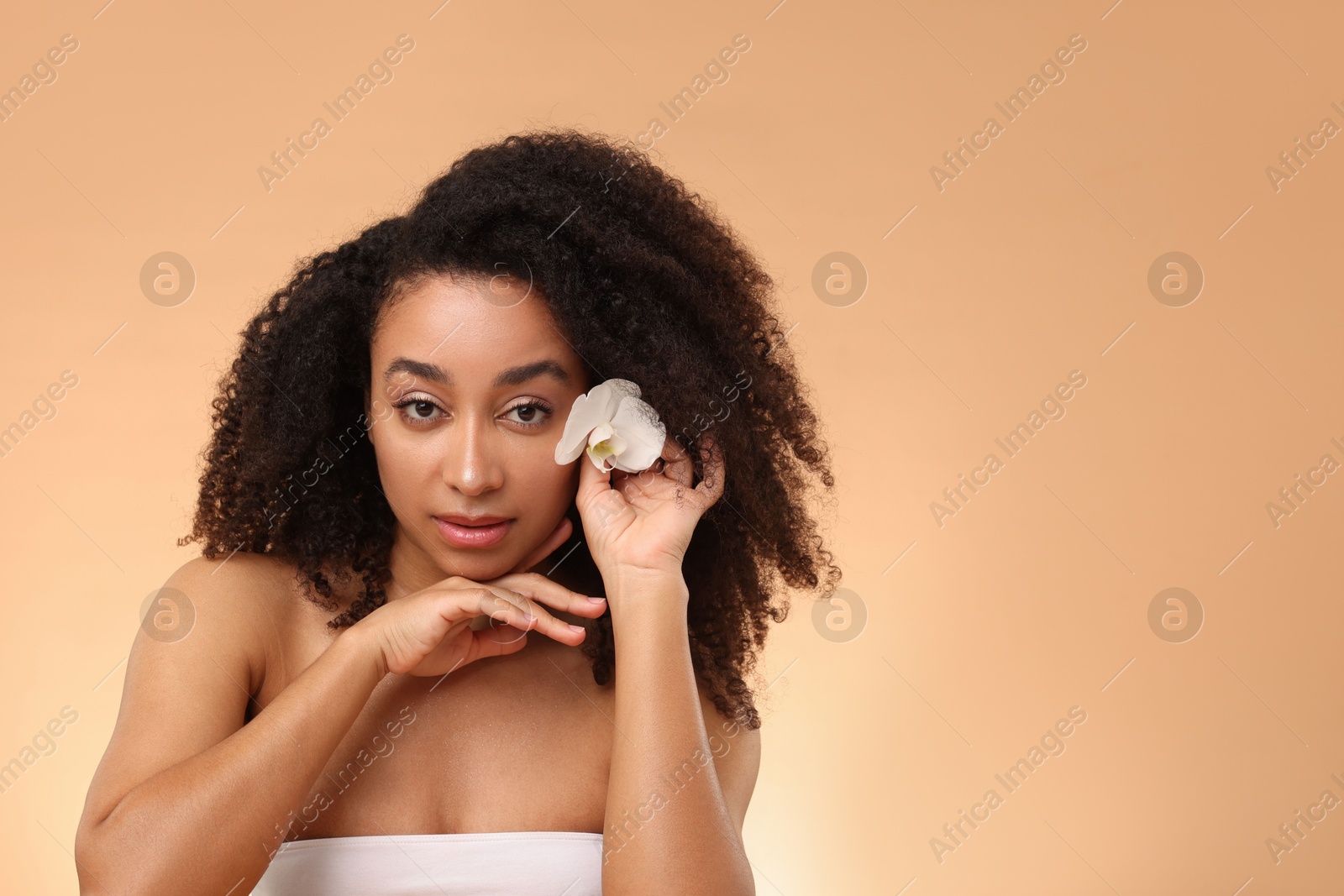 Photo of Portrait of beautiful Brazilian woman with orchid flower after spa treatment on beige gradient background. Space for text