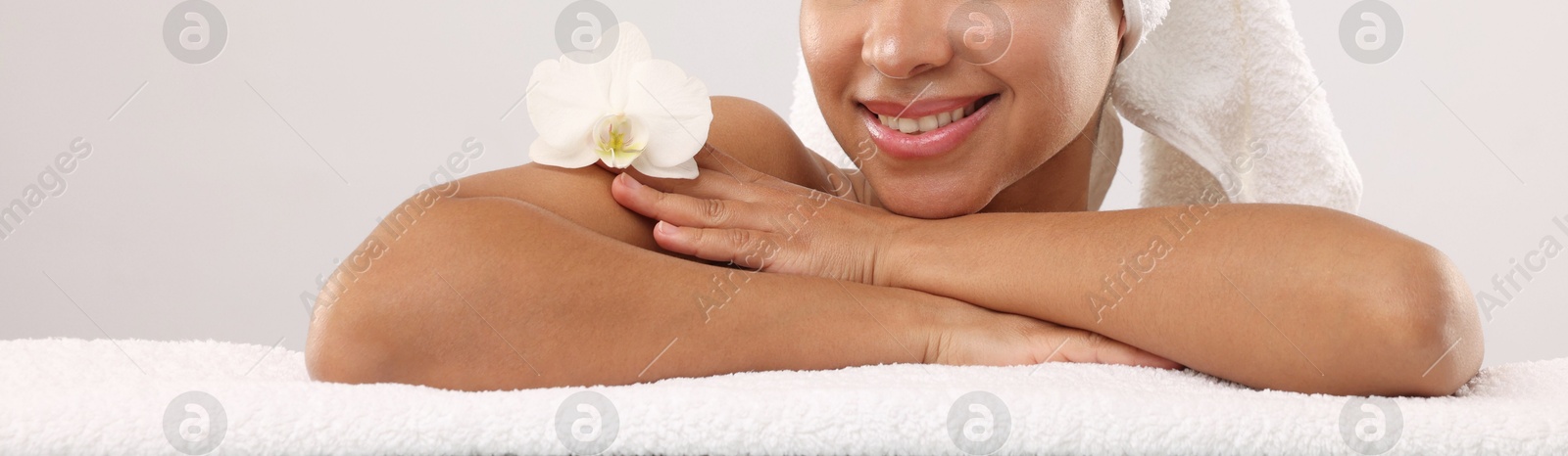 Photo of Brazilian woman with towel and orchid flower after spa treatment on light gray background, closeup