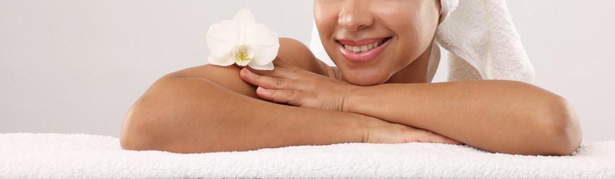 Photo of Brazilian woman with towel and orchid flower after spa treatment on light gray background, closeup
