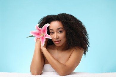 Photo of Portrait of beautiful Brazilian woman with lily flower and towel after spa treatment on light blue background