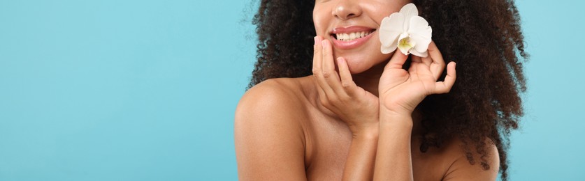 Photo of Brazilian woman with orchid flower after spa treatment on light blue background, closeup. Space for text