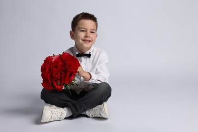 Photo of Smiling little boy with bouquet of beautiful flowers on light background