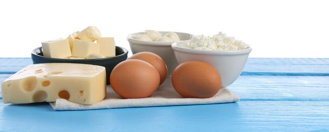 Photo of Different dairy products and eggs on blue wooden table against white background