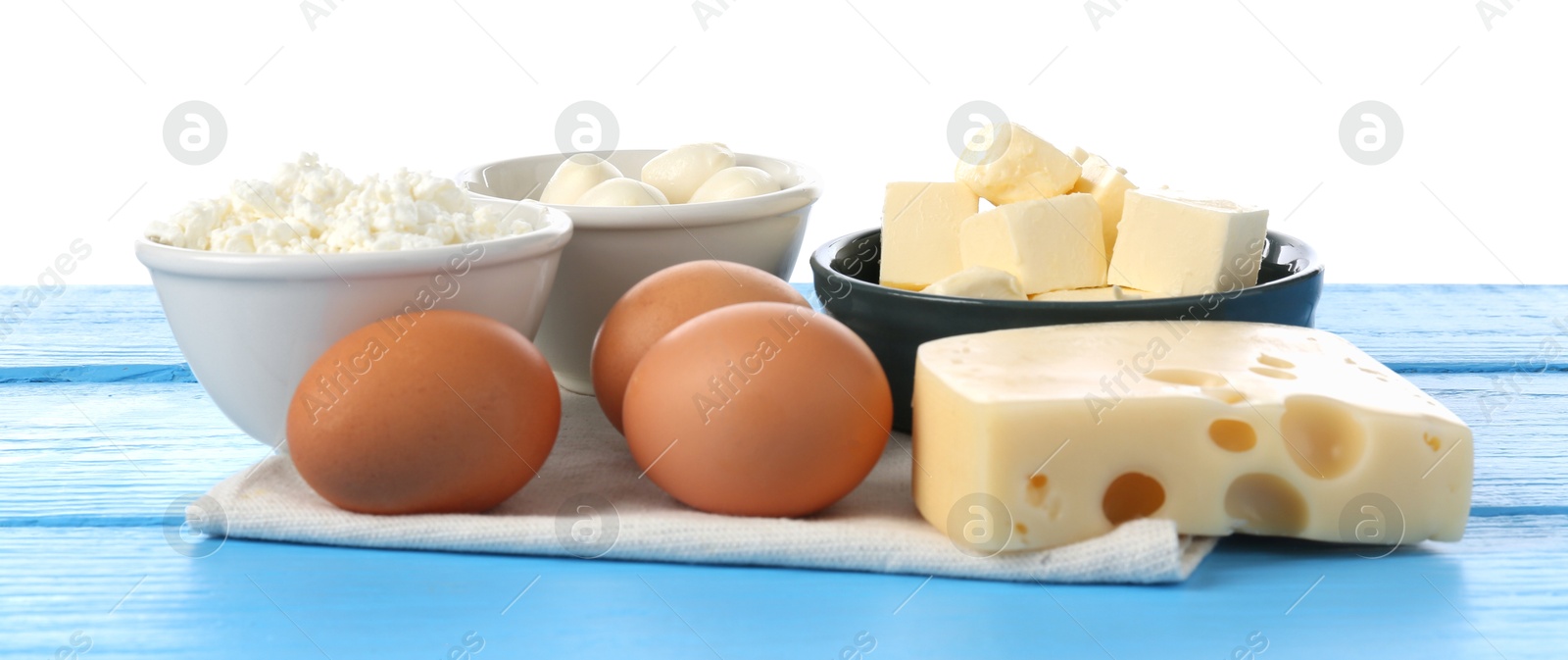 Photo of Different dairy products and eggs on blue wooden table against white background
