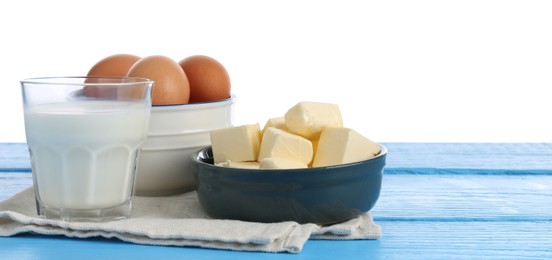 Photo of Milk, butter and eggs on blue wooden table against white background