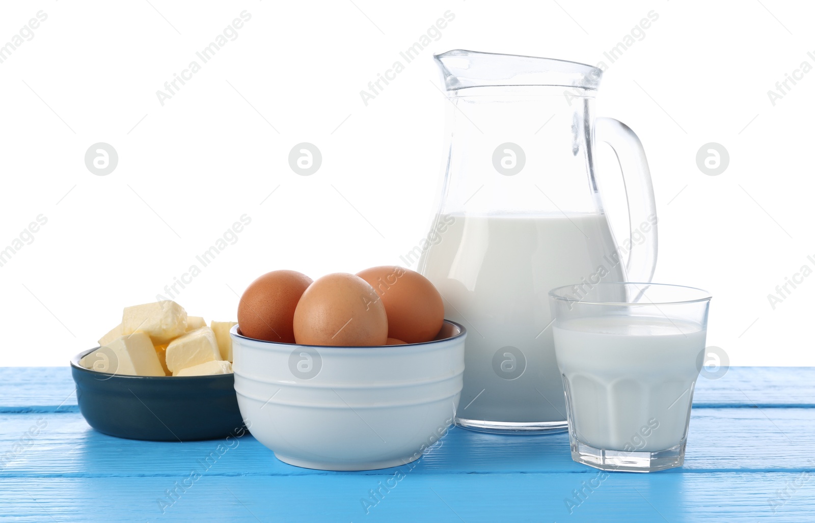 Photo of Milk, butter and eggs on blue wooden table against white background