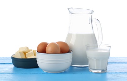 Photo of Milk, butter and eggs on blue wooden table against white background