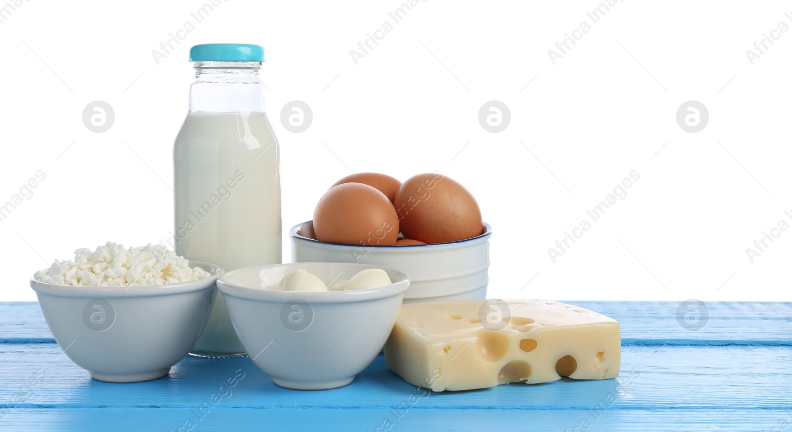 Photo of Different dairy products and eggs on blue wooden table against white background