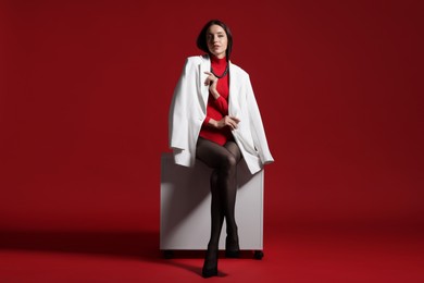 Photo of Full-length portrait of beautiful woman in stylish outfit and cabinet on red background