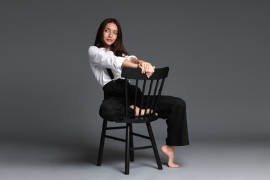 Photo of Beautiful woman in stylish outfit sitting on chair against grey background